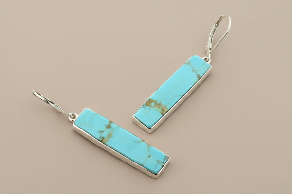 Turquoise bar earrings with silver hooks on a gray background