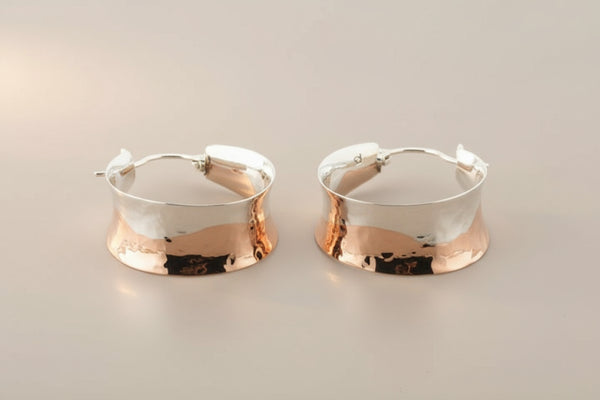 Pair of silver hoop earrings with copper accents on a gray background
