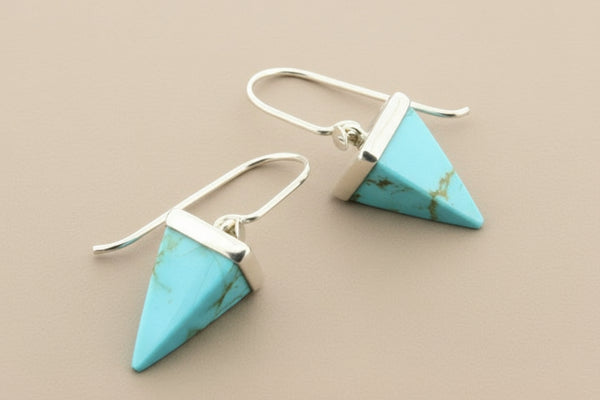 Turquoise triangle earrings with silver hooks on a gray background