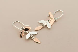 Pair of silver and rose gold leaf-shaped earrings on a dark gray background