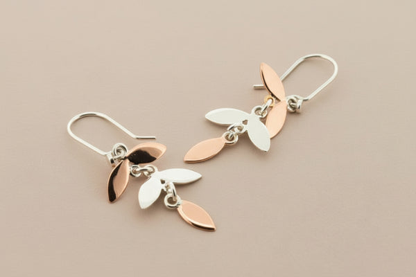 Pair of silver and rose gold leaf-shaped earrings on a dark gray background