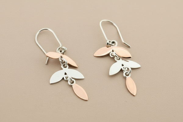 Pair of silver and rose gold leaf-shaped earrings on a gray background
