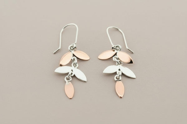 Pair of silver and rose gold leaf-shaped earrings on a gray background