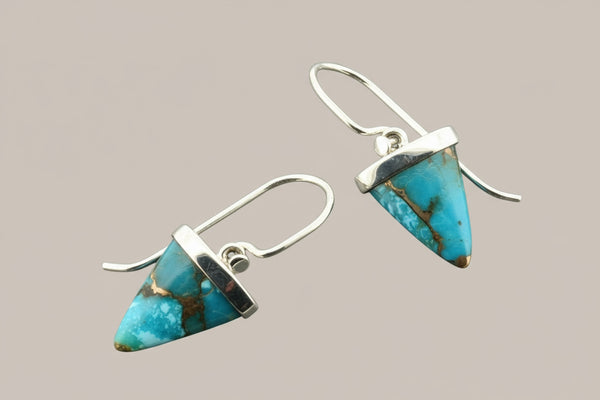 Turquoise triangle earrings with silver hooks on a gray background