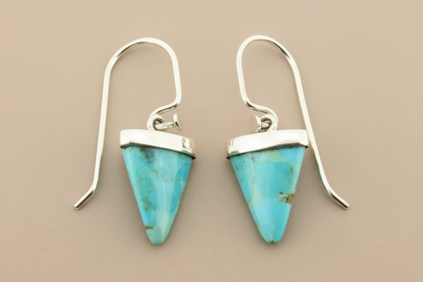 Turquoise triangle earrings with silver hooks on a gray background