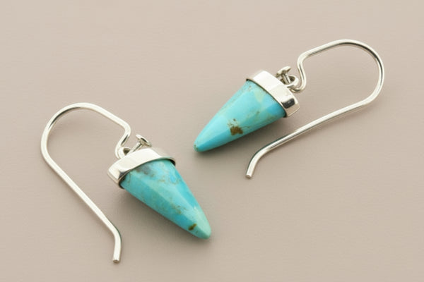Turquoise cone-shaped earrings with silver hooks on a gray background