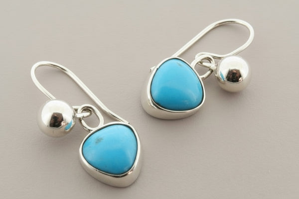 Pair of silver earrings with turquoise stones on a gray background
