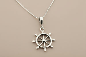 Silver ship's wheel pendant on a chain against a gray background