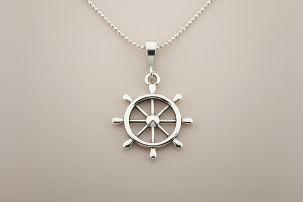 Silver ship's wheel pendant on a chain against a gray background