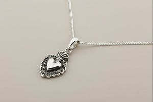 Silver heart-shaped pendant on a chain against a gray background