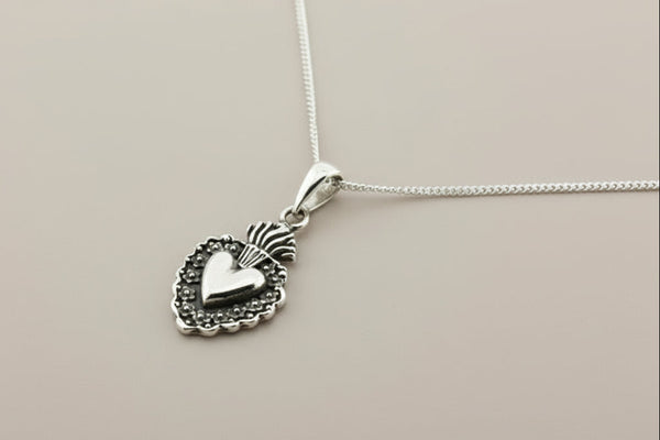 Silver heart-shaped pendant on a chain against a gray background