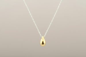Gold teardrop pendant on a silver chain against a gray background