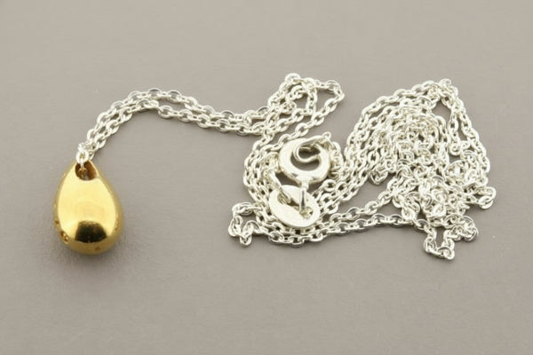 Gold teardrop pendant on a silver chain against a gray background