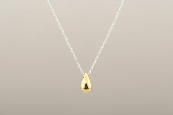 Gold teardrop pendant on a silver chain against a gray background