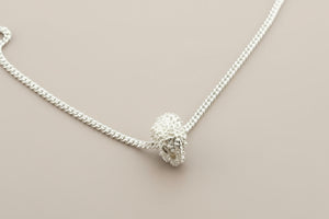 Silver necklace with a textured pendant on a gray background