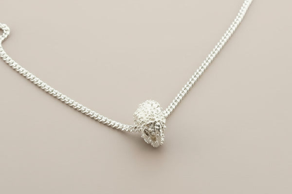 Silver necklace with a textured pendant on a gray background