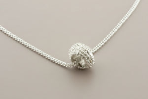 Silver necklace with a textured spherical pendant on a gray background