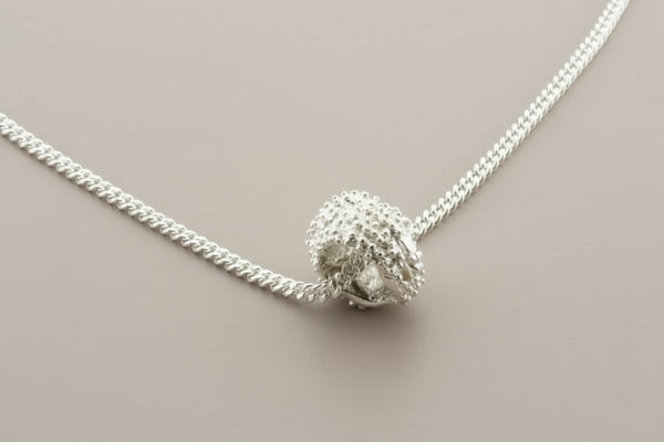 Silver necklace with a textured spherical pendant on a gray background