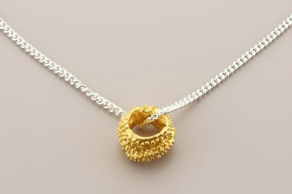Gold pendant on a silver chain against a gray background