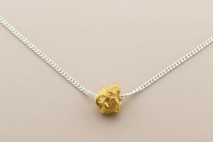 Gold necklace pendant on a silver chain against a gray background