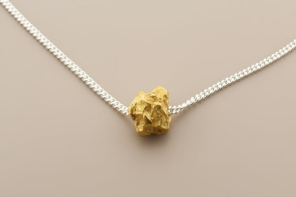 Gold nugget pendant on a silver chain against a gray background