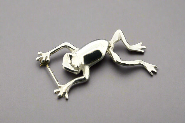 Silver frog brooch on a dark gray background