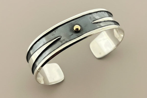 Silver bracelet with a gold accent on a dark gray background
