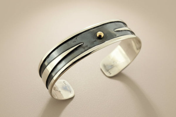 Silver bracelet with a central gold bead on a dark gray background