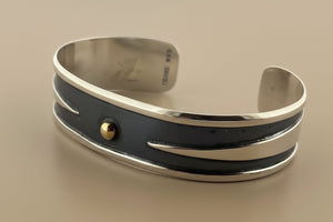 Silver bracelet with a central gold bead on a gray background