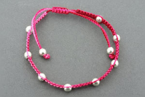Pink macrame bracelet with silver beads on a gray background