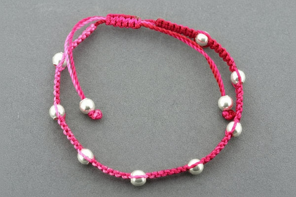 Pink macrame bracelet with silver beads on a gray background