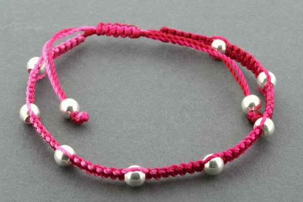 Pink macrame bracelet with silver beads on a gray background