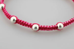 Pink macrame bracelet with silver beads on a gray background
