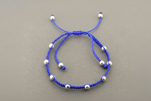 Blue braided bracelet with silver beads on a gray background