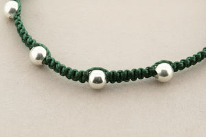Green macrame bracelet with silver beads on a gray background