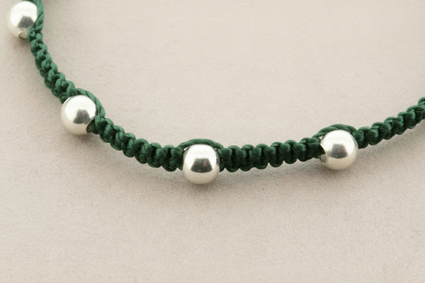 Green macrame bracelet with silver beads on a gray background