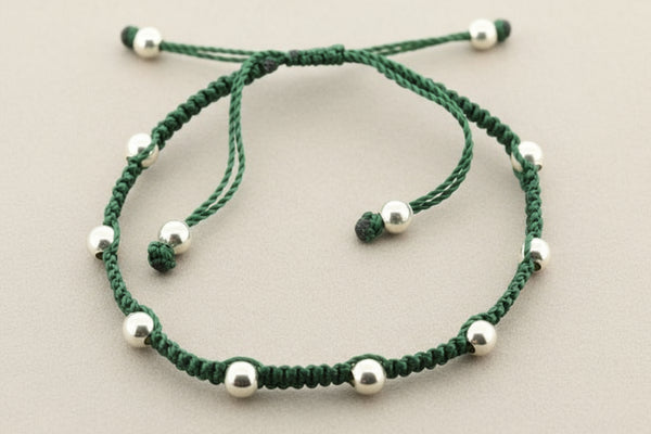 Green macrame bracelet with silver beads on a gray background