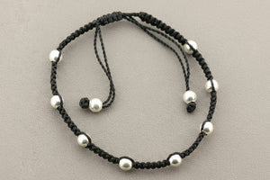 Black cord bracelet with silver beads on a gray background