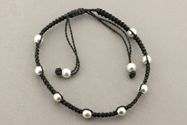 Black cord bracelet with silver beads on a gray background