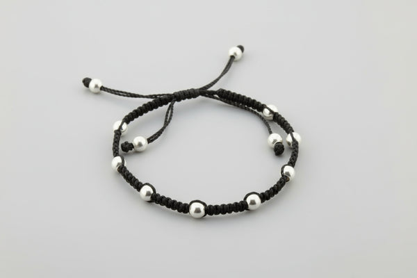 Black macrame bracelet with silver beads on a gray background