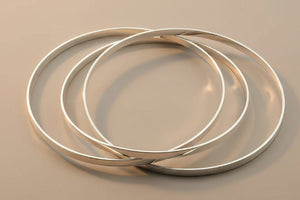 Three silver bangles stacked on a gray surface