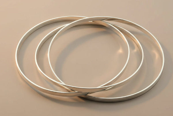 Three silver bangles stacked on a gray surface