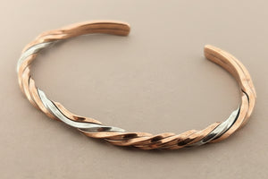 Twisted rose gold and silver bracelet on a gray background