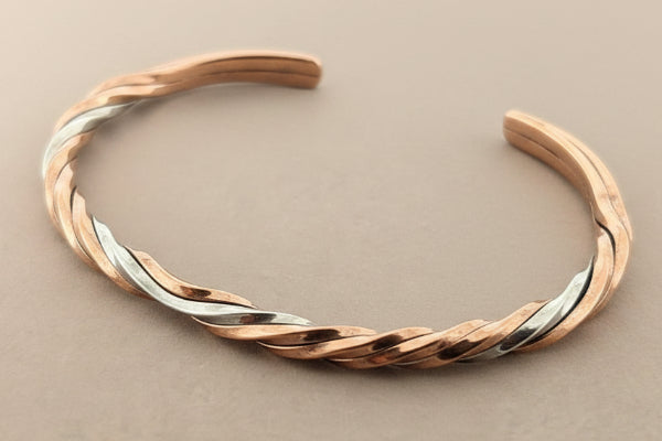 Twisted rose gold and silver bracelet on a gray background