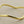 Load image into Gallery viewer, A polished gold-toned metal bangle bracelet with a wavy, organic silhouette, displayed on a textured dark gray background.
