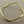 Load image into Gallery viewer, A polished gold-toned metal cuff bracelet with a wavy, organic silhouette, displayed on a textured gray background.
