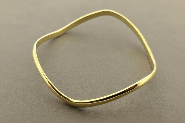 A polished gold-toned metal cuff bracelet with a wavy, organic silhouette, displayed on a textured gray background.