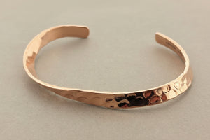 A hammered copper cuff bracelet with a textured, organic surface, displayed on a neutral gray background.