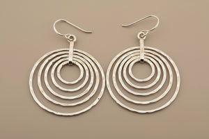 Pair of silver hoop earrings with concentric circles on a dark background