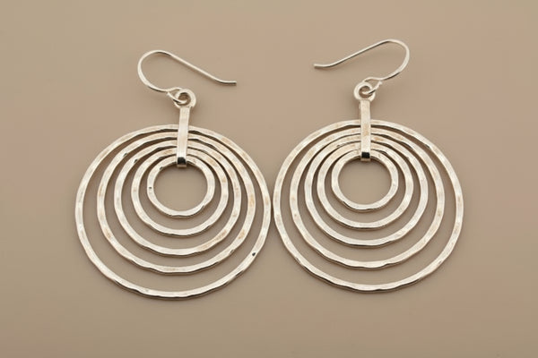 Pair of silver hoop earrings with concentric circles on a dark background